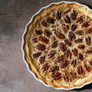 Ganzer klassischer Pecan Pie in heller Form von oben, dicht mit Pekannusshälften belegt in goldbrauner Füllung