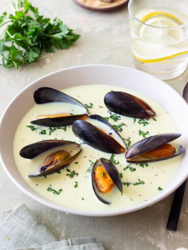 Cremige Muschelsuppe mit ganzen Miesmuscheln und gehackter Petersilie in einer weißen Schale, Nahaufnahme von der Seite
