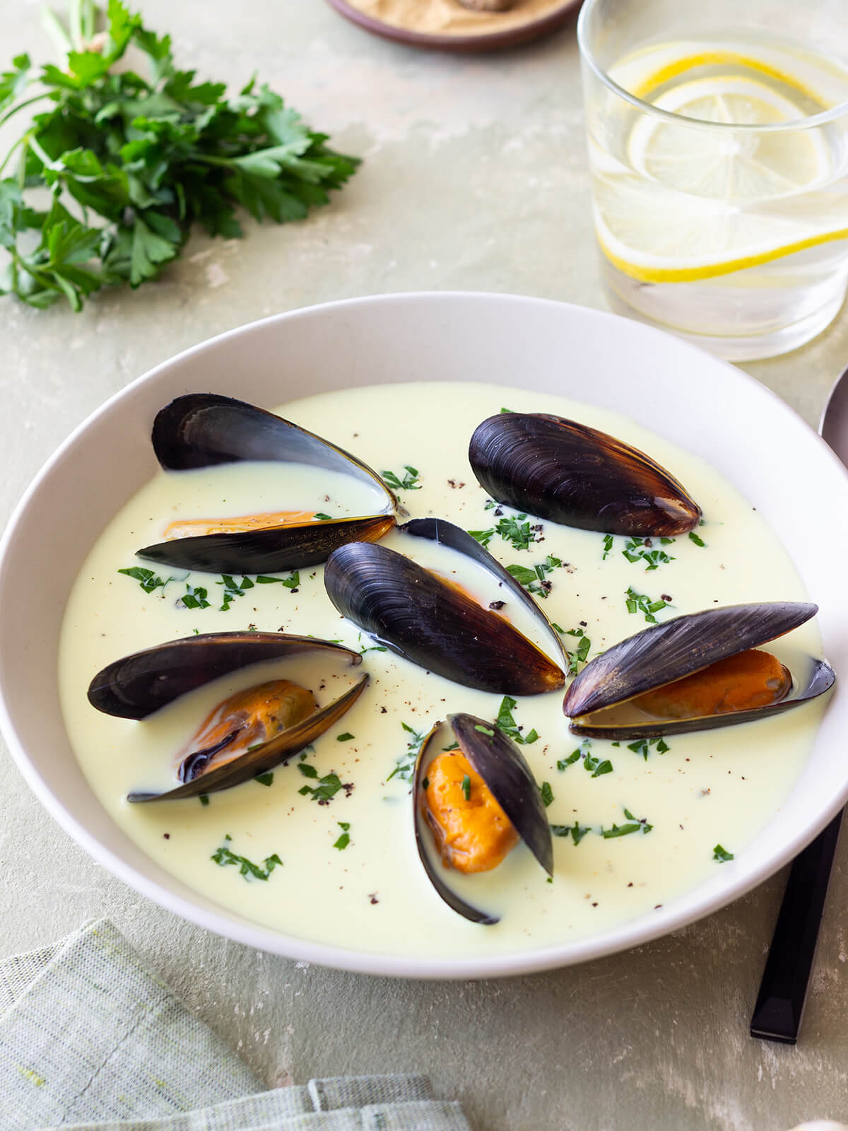 Cremige Muschelsuppe mit ganzen Miesmuscheln und gehackter Petersilie in einer weißen Schale, Nahaufnahme von der Seite