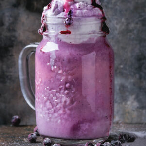 Cremiger Blaubeer-Smoothie im Henkelglas mit Sahnehaube, Blaubeersauce und gefrorenen Blaubeeren
