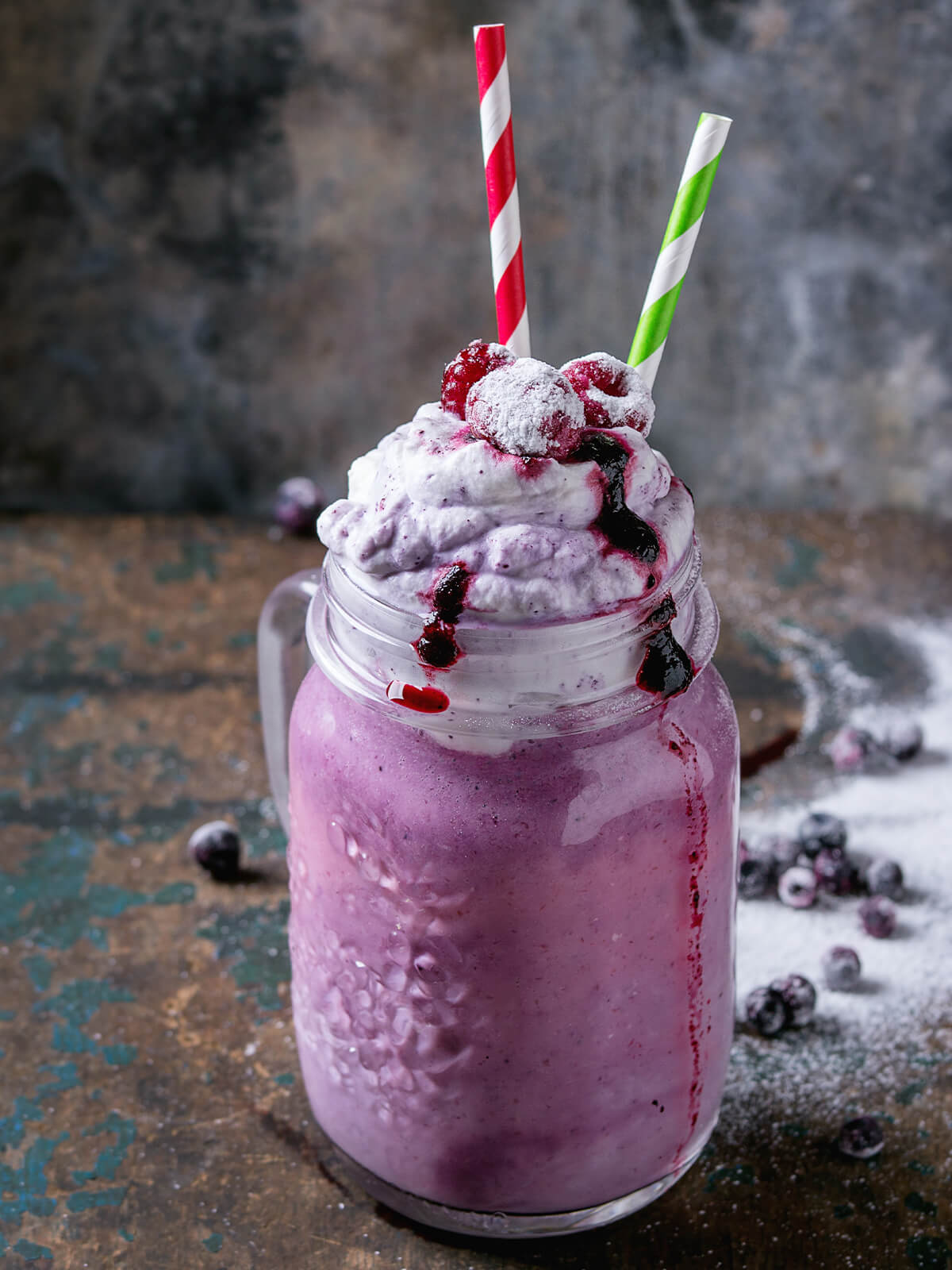 Cremiger Blaubeer-Smoothie mit Sahnehaube und Blaubeersauce, garniert mit gefrorenen Beeren und Puderzucker