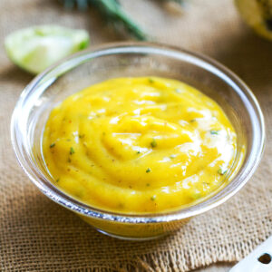 Cremiges gelbes Mango-Dressing in einer Glasschale mit Limette und Rosmarin auf einer Jutematte