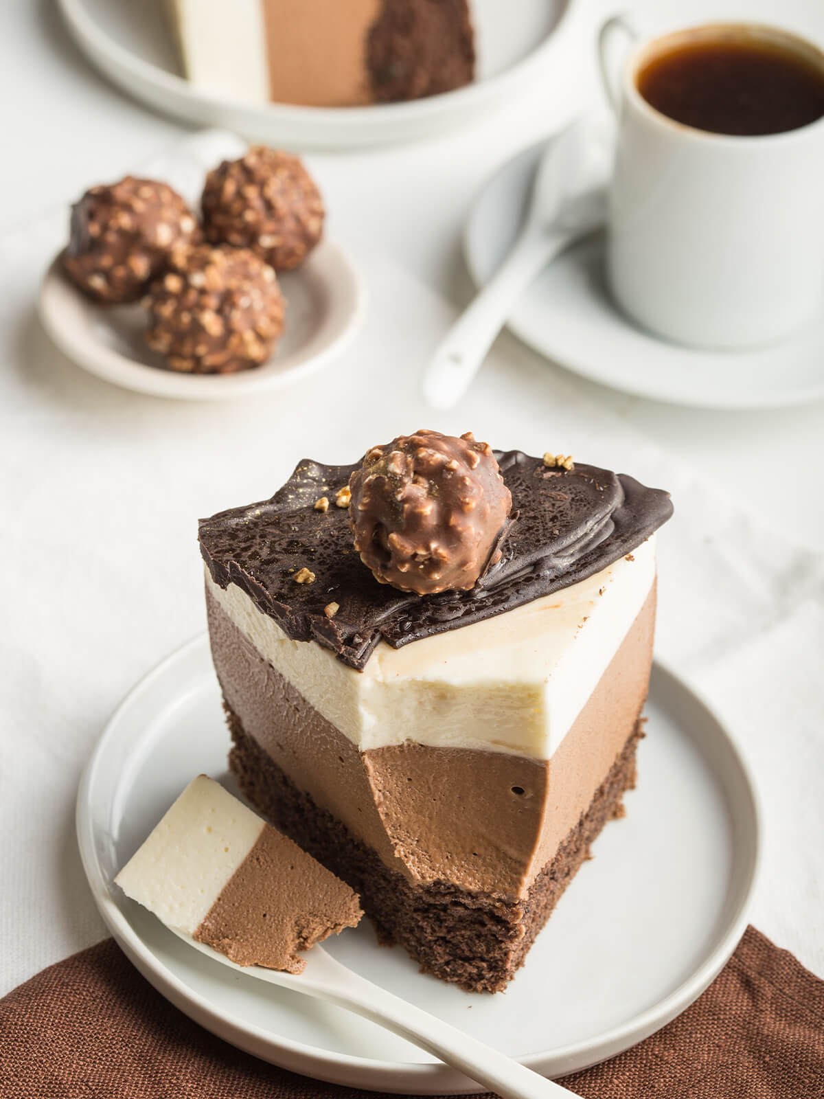 Ein Stück Schokoladen-Mousse-Torte mit dunklem Boden, zwei Mousse-Schichten und Schoko-Haselnuss-Kugel auf einem Teller