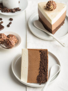 Zwei Stücke Drei-Schokoladen-Mousse-Torte auf Tellern, die drei Mousse-Schichten und der Biskuitboden sind deutlich sichtbar