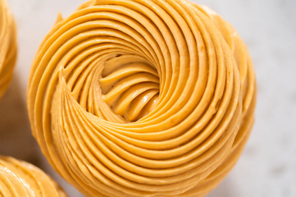 Karamellfarbene Dulce-de-Leche-Buttercreme als feiner Rosenwirbel auf einem Cupcake in Nahaufnahme