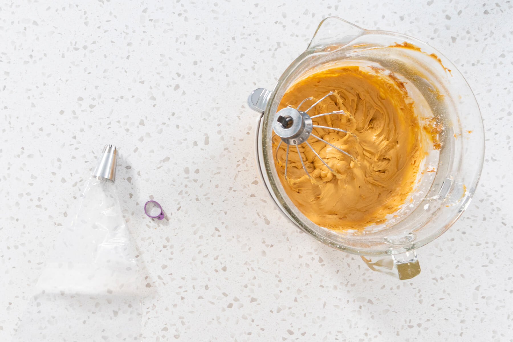 Rührschüssel mit karamellfarbener Buttercreme neben einem leeren Spritzbeutel und einer Sterntülle von oben