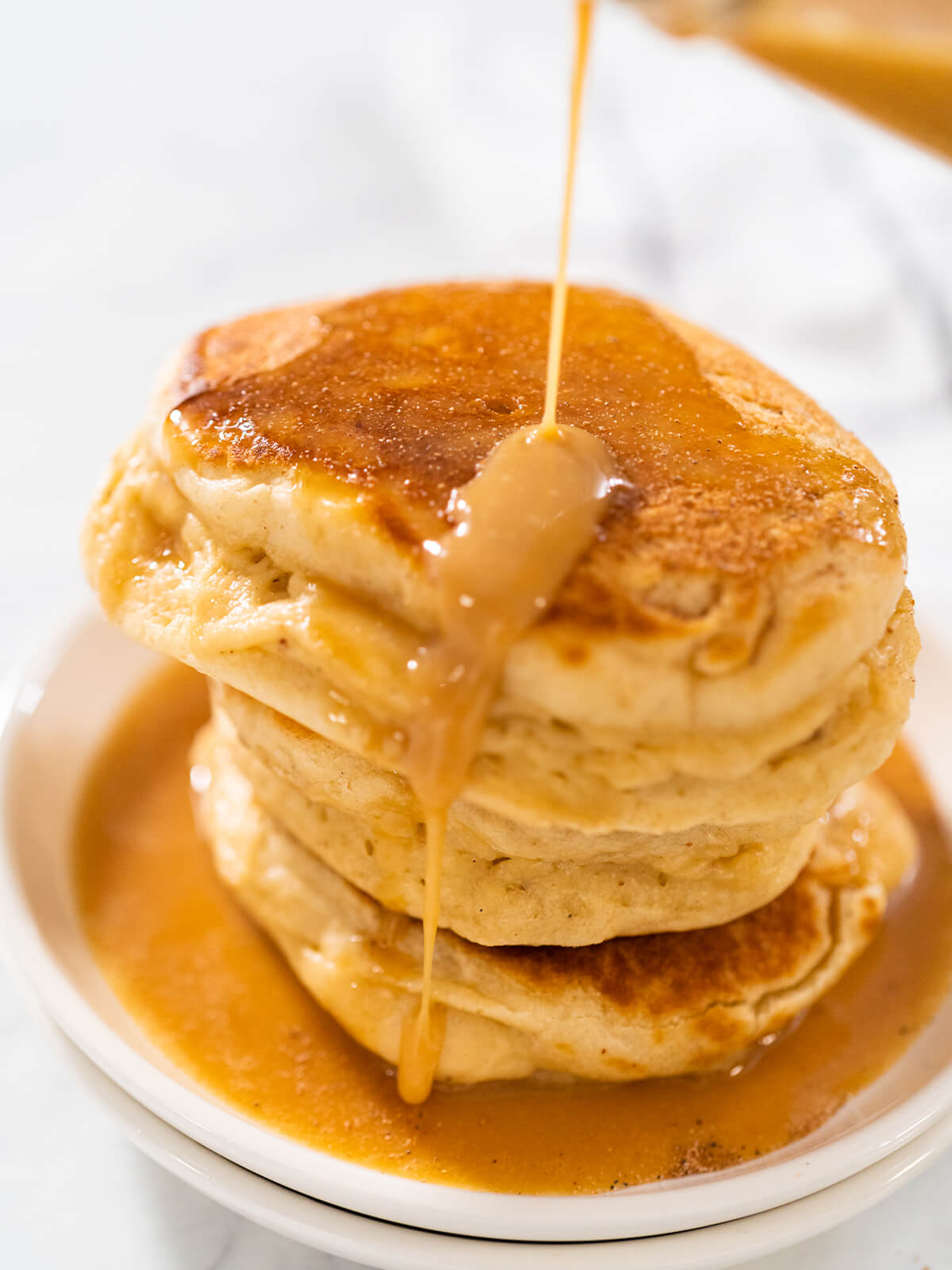 Ein hoher Stapel fluffiger Eierlikör-Pfannkuchen, übergossen mit warmer Eierlikör-Karamellsauce, auf einem weißen Teller