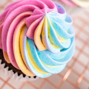 Regenbogen-Buttercreme in Rosa, Blau, Gelb und Violett als Wirbel auf einem Schokoladen-Cupcake von oben