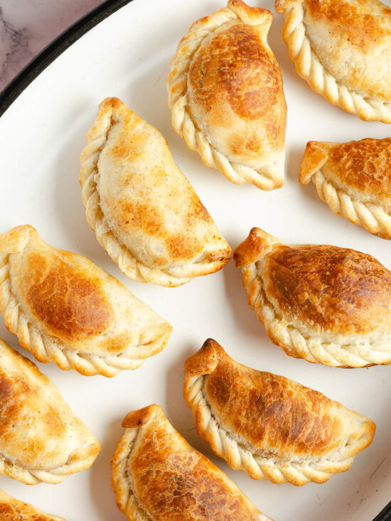 Goldbraun gebackene argentinische Rindfleisch-Empanadas mit geflochtenem Rand auf einer weißen Platte