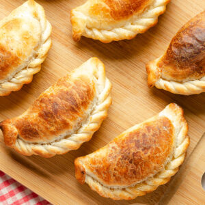 Goldbraun gebackene argentinische Rindfleisch-Empanadas mit geflochtenem Rand auf einem Holzbrett