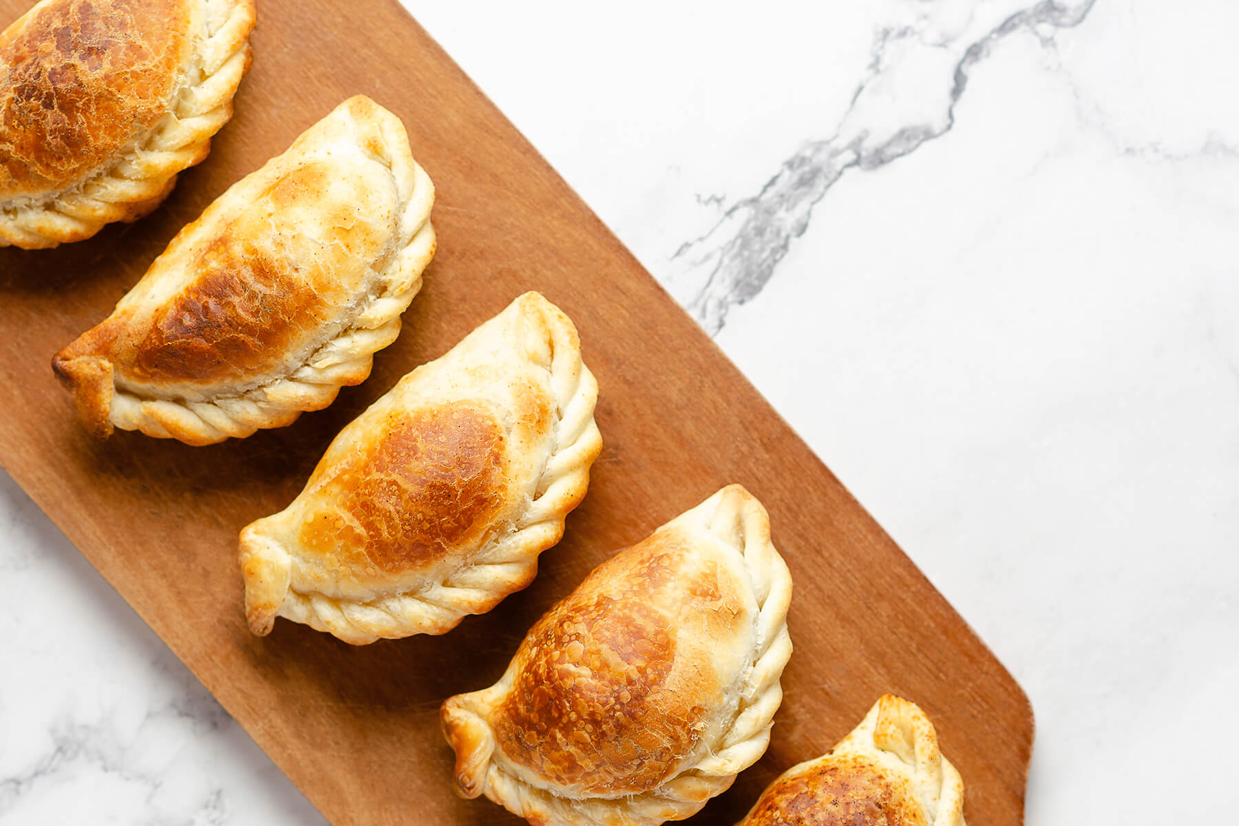 Mehrere gebackene argentinische Empanadas mit geflochtenem Rand in einer Reihe auf einem Holzbrett