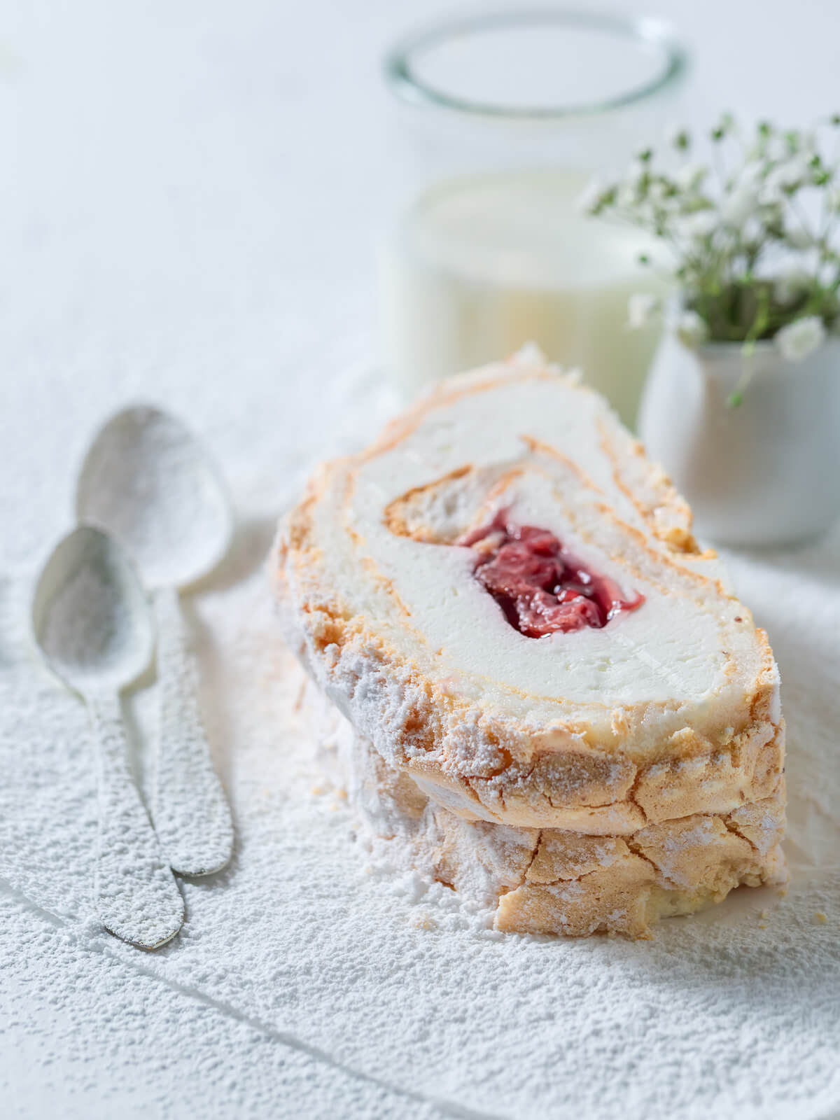 Stück Baiser-Roulade mit Sahne und leuchtendem Erdbeer-Fruchtkern im Anschnitt, mit Puderzucker bestäubt