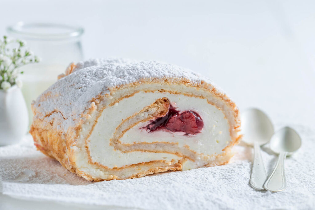 Angeschnittene Baiser-Roulade mit Sahne und Erdbeer-Füllung, Puderzucker bestäubt, mit sichtbarer Spirale
