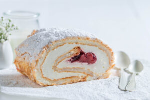 Angeschnittene Baiser-Roulade mit Sahne und Erdbeer-Füllung, Puderzucker bestäubt, mit sichtbarer Spirale