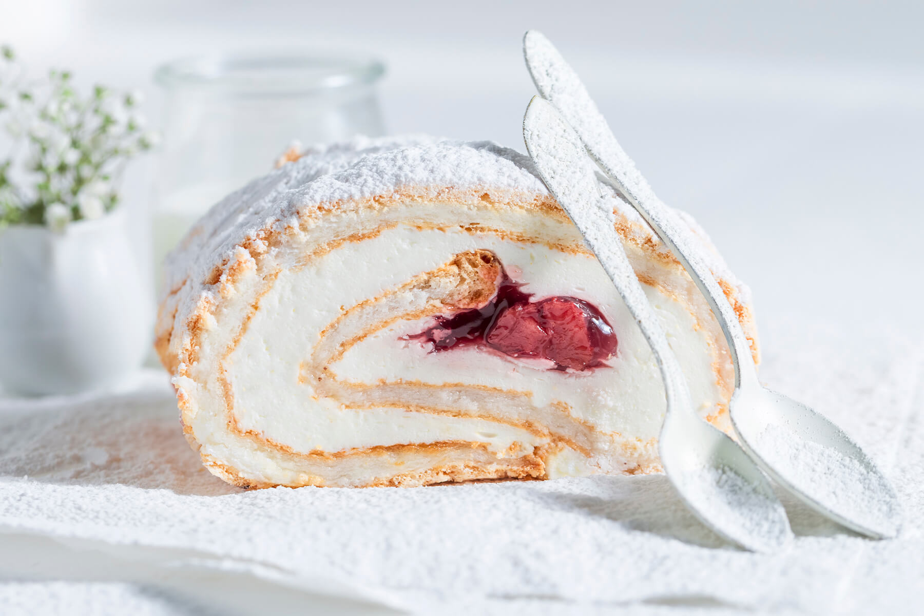 Angeschnittene Baiser-Roulade mit Sahnefüllung und rotem Erdbeer-Fruchtkern, mit Puderzucker bestäubt