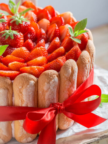 Erdbeer-Charlotte mit Löffelbiskuit-Kranz, dicht mit frischen Erdbeeren belegt und mit rotem Band