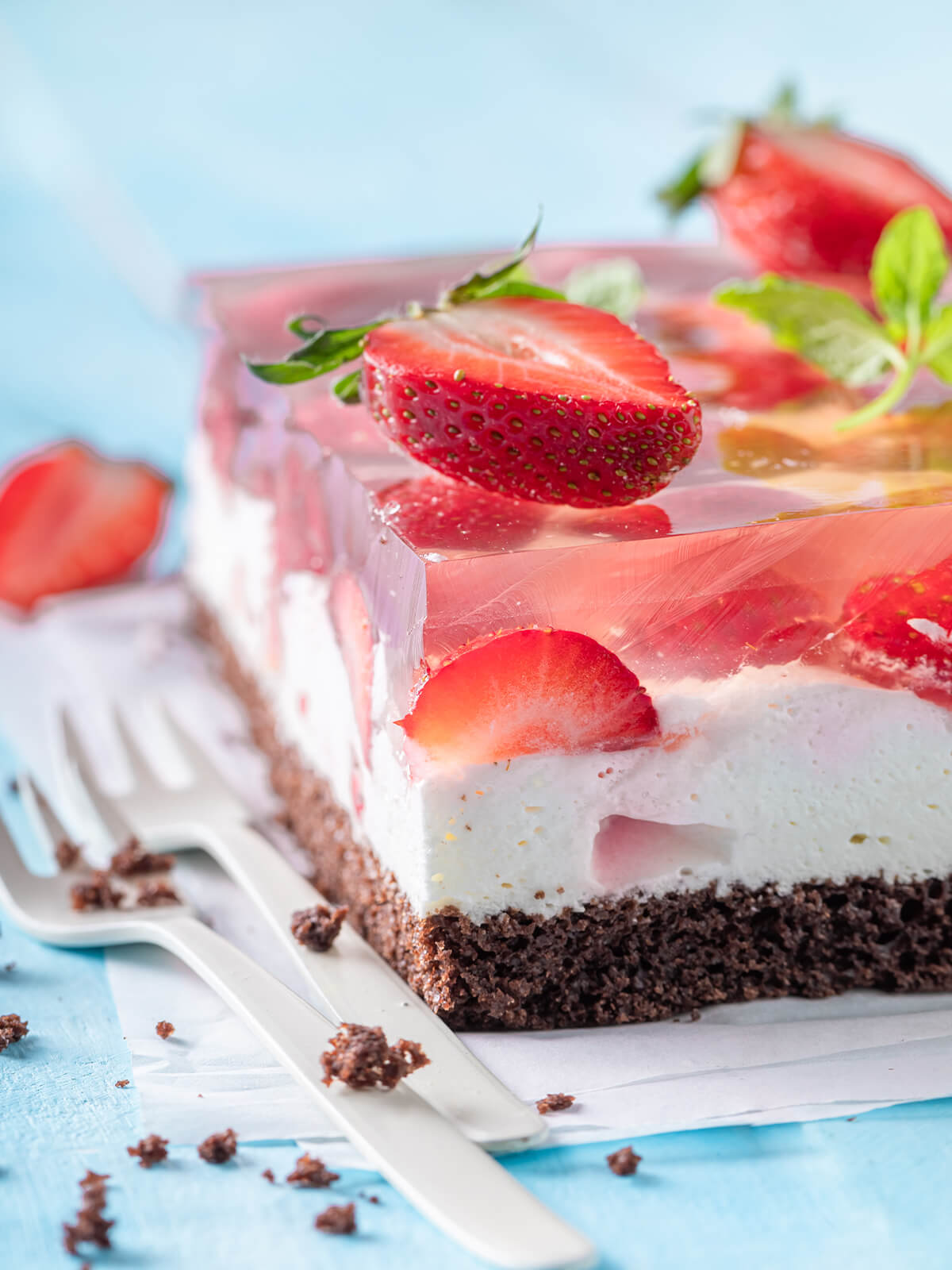 Angeschnittene Erdbeer-Gelee-Schnitte mit dunklem Schokoboden, weißer Sahnecreme und glasklarem Gelee mit halbierten Erdbeeren