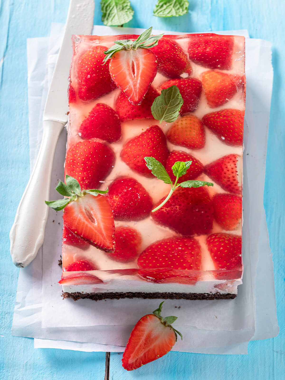 Blechkuchen von oben, dicht belegt mit halbierten Erdbeeren unter durchsichtigem Gelee, dazwischen schimmert die weiße Creme durch, garniert mit Minze