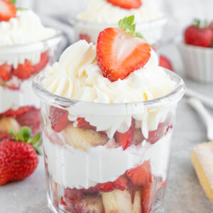Erdbeer-Tiramisu im Glas mit Schichten aus Löffelbiskuits, Mascarponecreme und Erdbeerscheiben, gekrönt von aufgespritzter Creme und einer halben Erdbeere