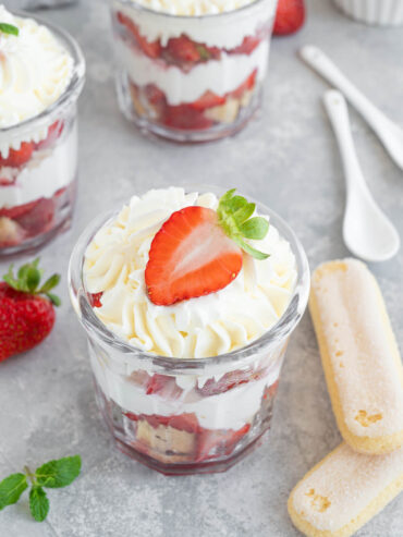 Erdbeer-Tiramisu im Glas von vorn mit sichtbaren Schichten aus Löffelbiskuits, Creme und Erdbeeren, dahinter weitere Gläser und Löffelbiskuits