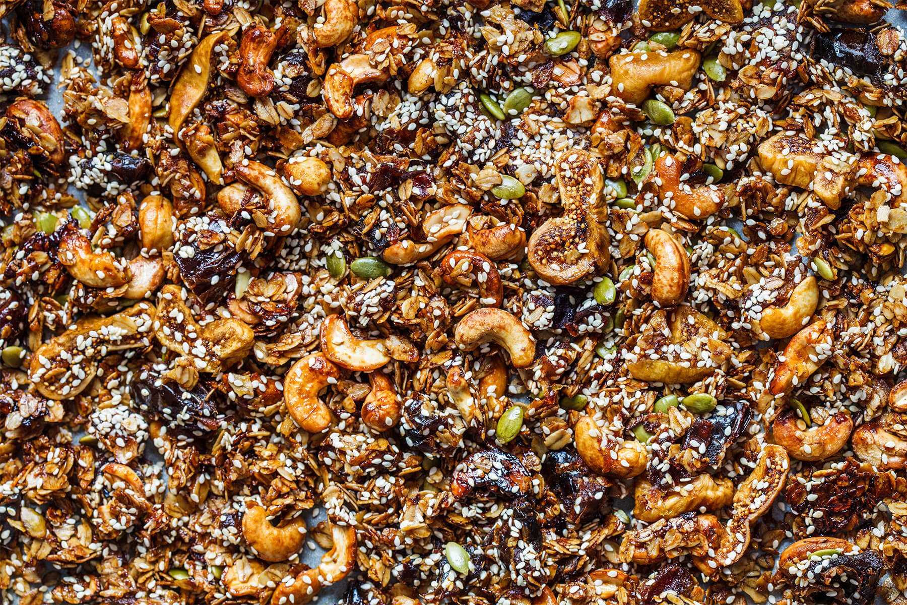 Nahaufnahme von knusprigem Granola mit ganzen Cashews, Sesam, Kürbiskernen sowie getrockneten Feigen und Datteln