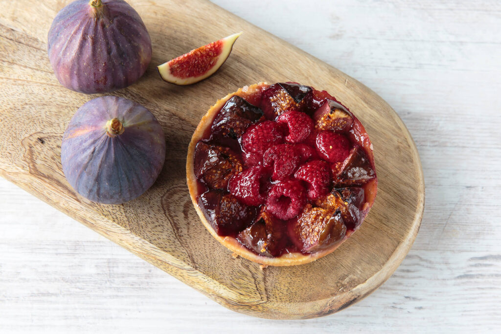 Feigen-Himbeer-Tartelette mit mitgebackenen Feigenspalten und Himbeeren, glänzend vom eingedickten Fruchtsaft, daneben frische Feigen
