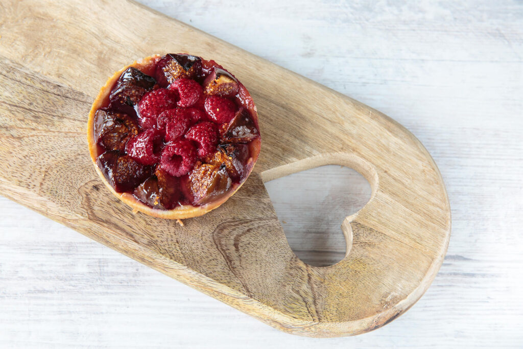 Fertiges Feigen-Himbeer-Tartelette mit dunkel gebackenen Feigenspalten und mitgebackenen Himbeeren auf einem Holzbrett