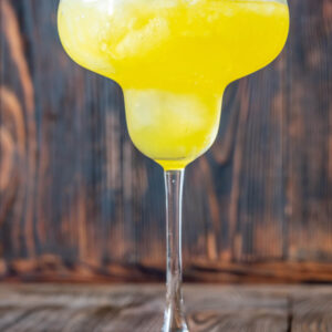 Sonnengelbe Frozen Banana Margarita im Margarita-Glas mit Salzrand auf dunklem Holz, cremig-slushige Konsistenz