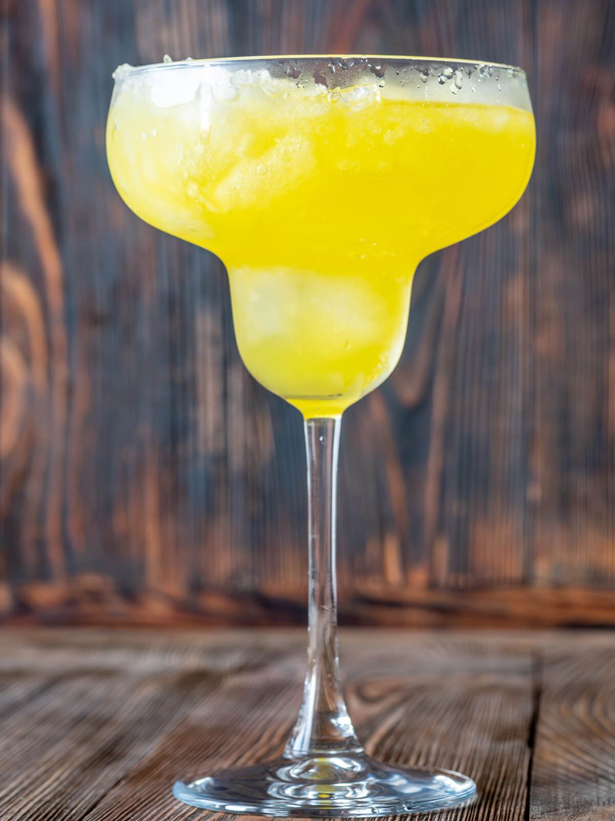 Sonnengelbe Frozen Banana Margarita im Margarita-Glas mit Salzrand auf dunklem Holz, cremig-slushige Konsistenz