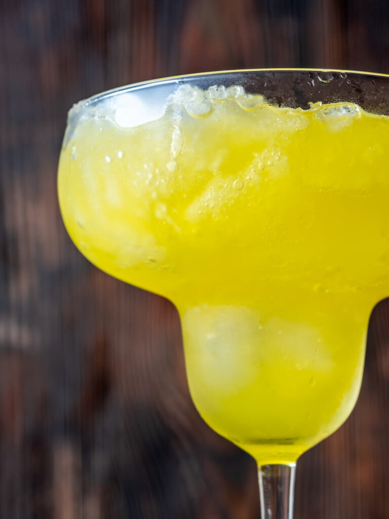 Nahaufnahme der cremig-slushigen, sonnengelben Frozen Banana Margarita im Glas mit Salzrand