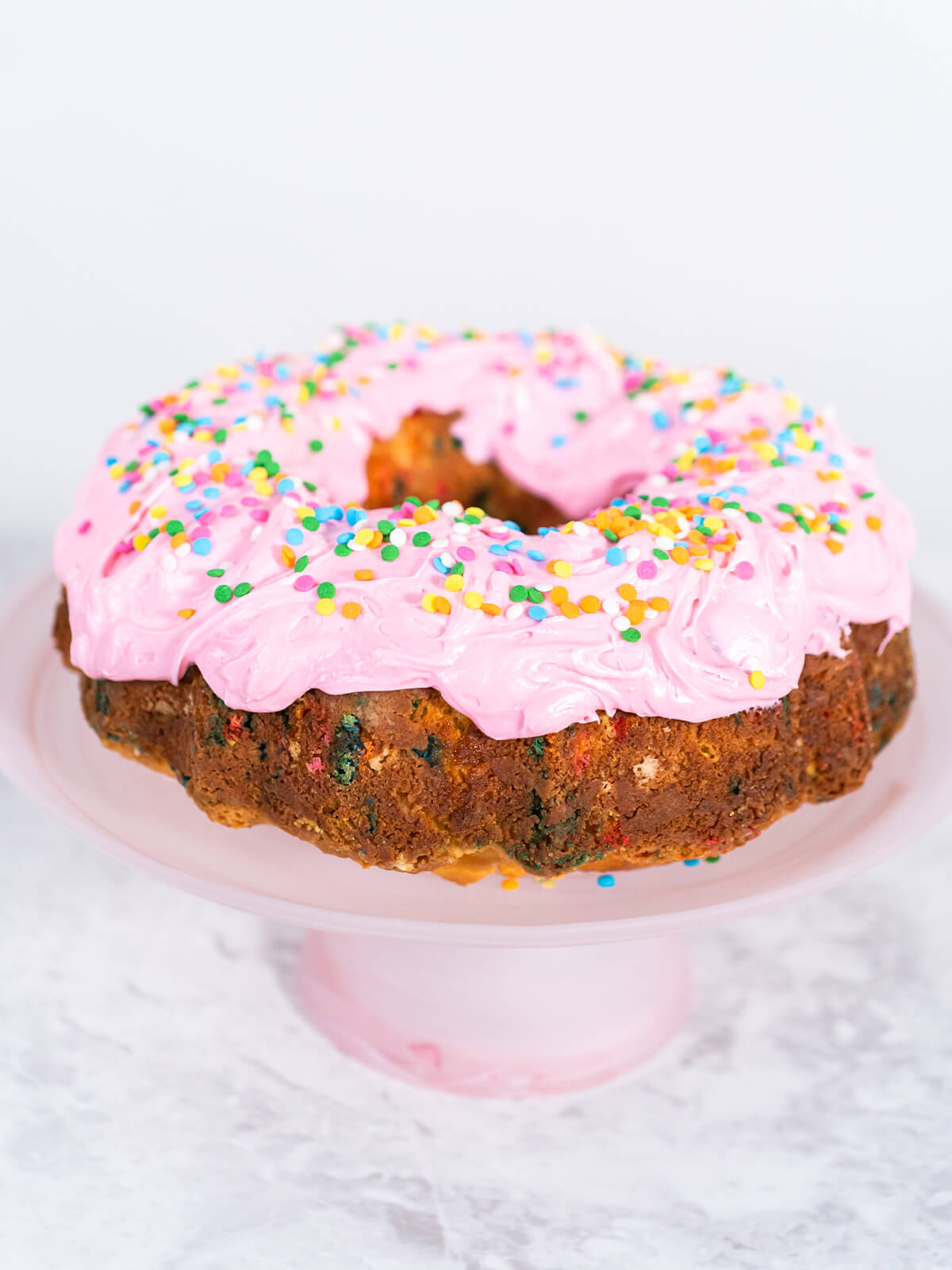Bunter Konfetti-Gugelhupf mit rosa Buttercreme und Konfetti-Streuseln auf einer rosa Kuchenplatte