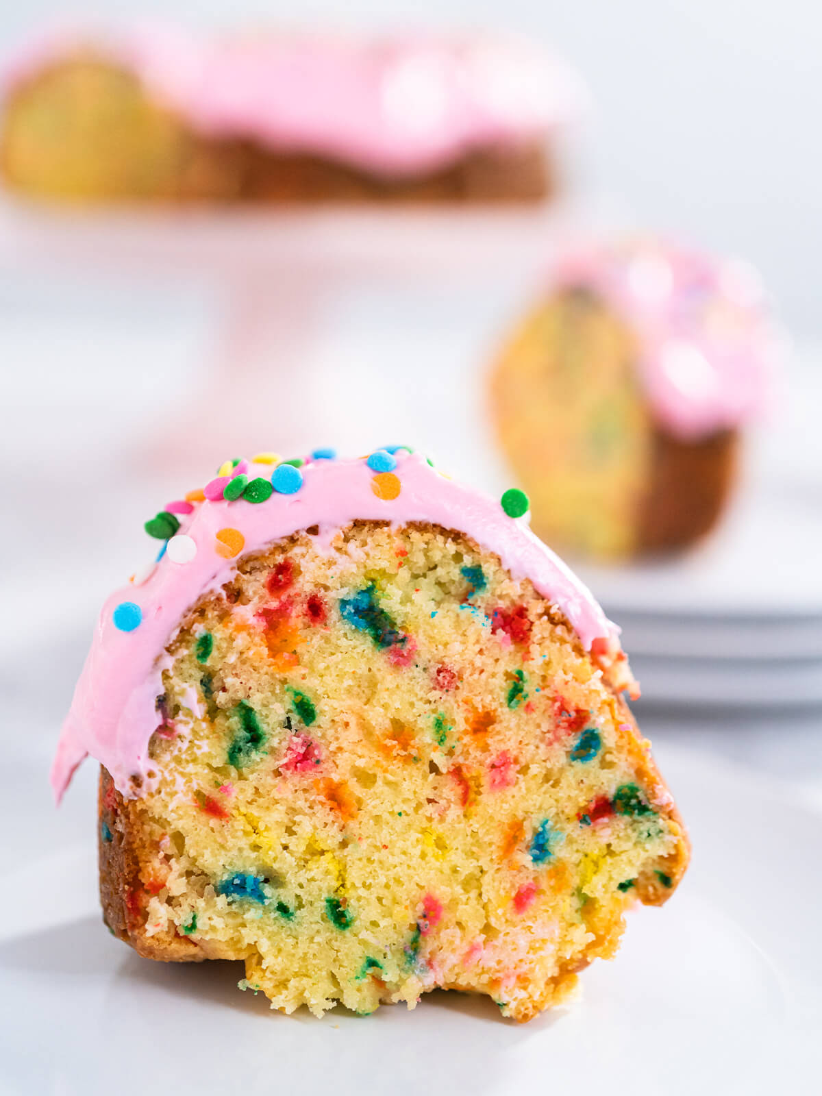 Angeschnittenes Stück Konfetti-Gugelhupf mit buntem Streuselteig und rosa Buttercreme auf einem Teller