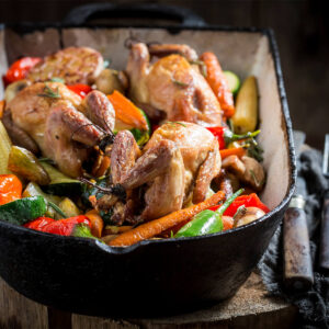 Gebackene Wachteln mit buntem Ofengemüse aus Karotten, Zucchini, Paprika, Maiskölbchen und Champignons in einer gusseisernen Form