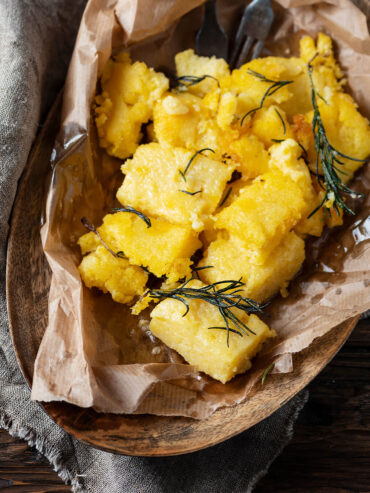 Gebratene Polenta-Stücke mit knusprigen Rändern und gebratenem Rosmarin in einer mit Papier ausgelegten Holzschale