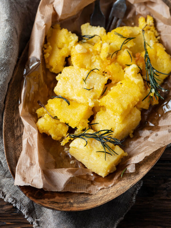 Gebratene Polenta-Stücke mit knusprigen Rändern und gebratenem Rosmarin in einer mit Papier ausgelegten Holzschale