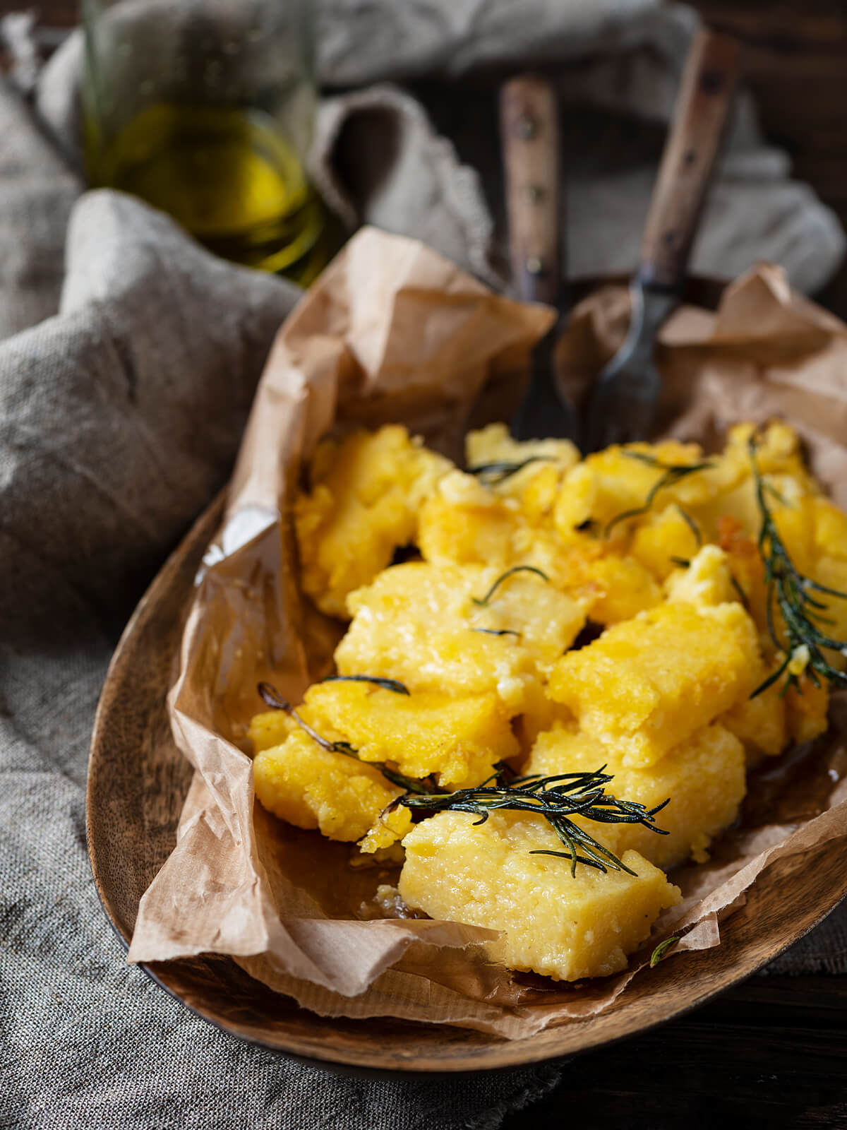 Gebratene Polenta-Stücke mit knusprigen Rändern und Rosmarin in einer Schale, daneben eine Flasche Olivenöl