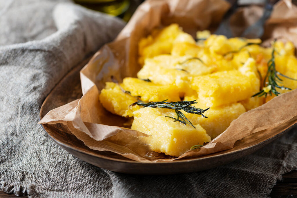 Gebratene Polenta-Stücke mit knusprigen Rändern und gebratenem Rosmarin in einer mit Papier ausgelegten Schale