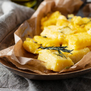 Gebratene Polenta-Stücke mit knusprigen Rändern und gebratenem Rosmarin in einer mit Papier ausgelegten Schale