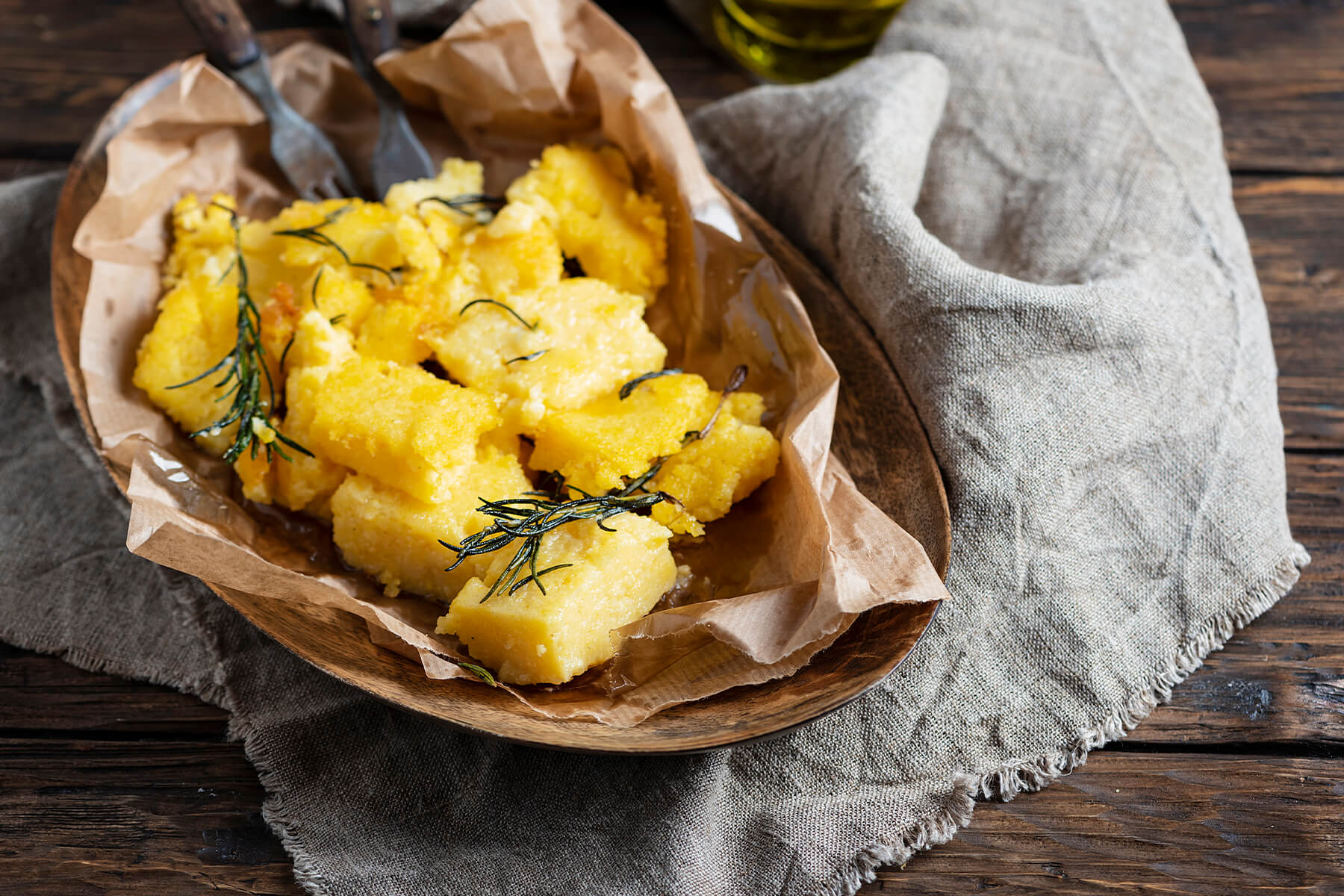 Nahaufnahme knusprig gebratener Polenta-Stücke mit gebratenem Rosmarin in einer rustikalen Schale