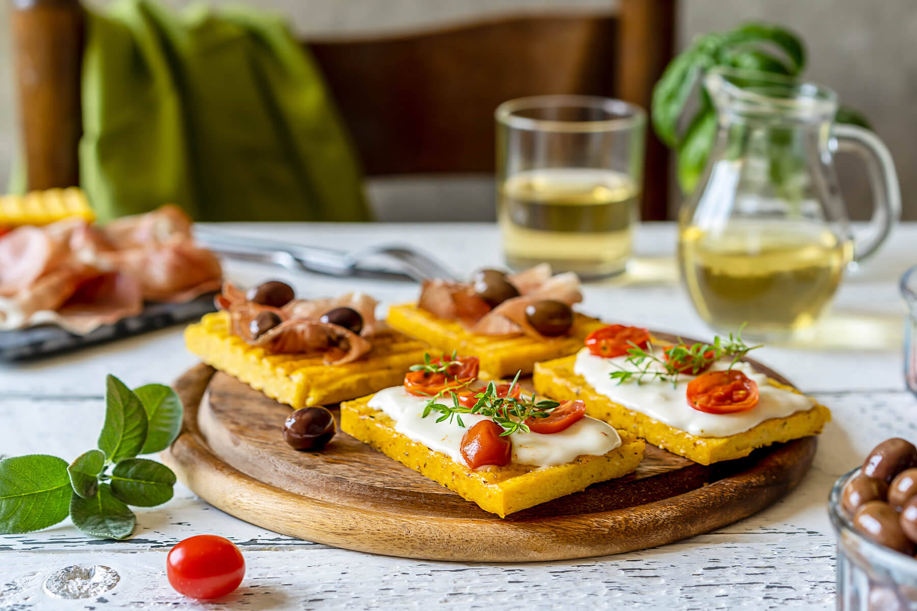 Gegrillte Polenta-Schnitten mit beiden Belägen auf einem Holzbrett, im Hintergrund Weißwein