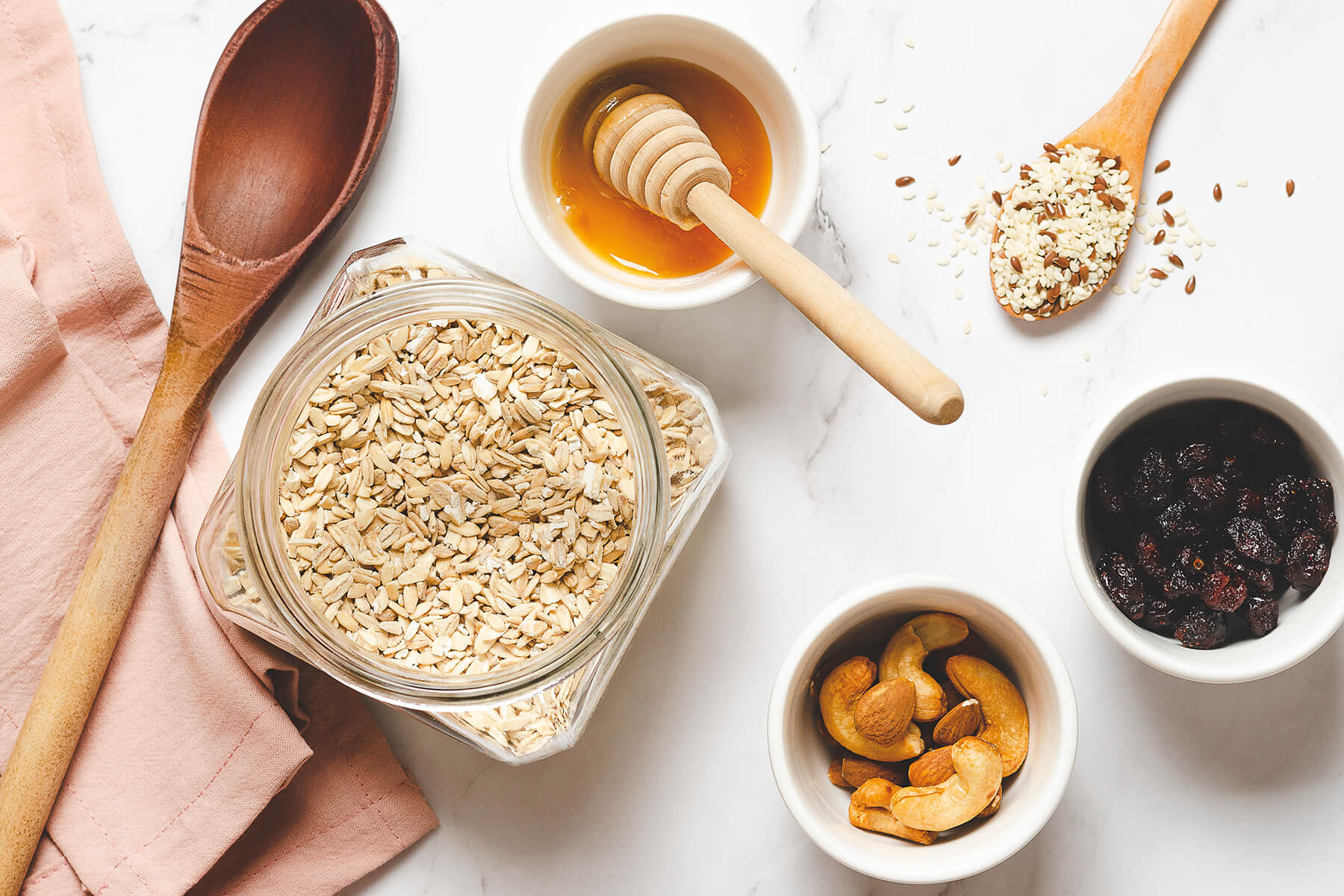 Zutaten für selbst gemachtes Granola – Haferflocken im Glas, Honig, Sesam, Leinsamen, Cashews und getrocknete Cranberries