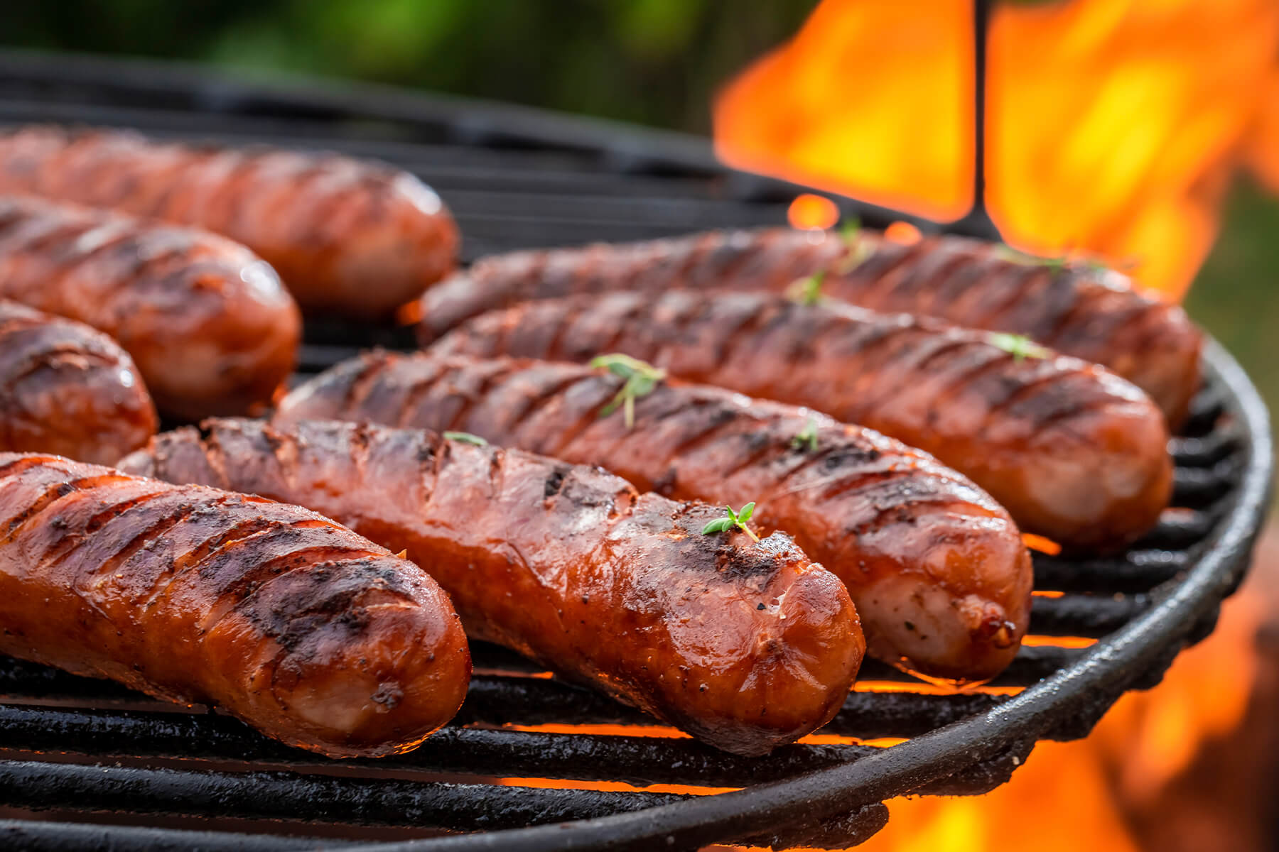 "Gegrillte Würste mit Grillstreifen auf dem Rost eines Holzkohlegrills über offenen Flammen"