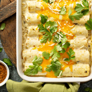 Cremige Hähnchen-Enchiladas von oben in einer weißen Auflaufform, weiße Sauce mit grünen Chilistückchen, geschmolzener Cheddar und frischer Koriander