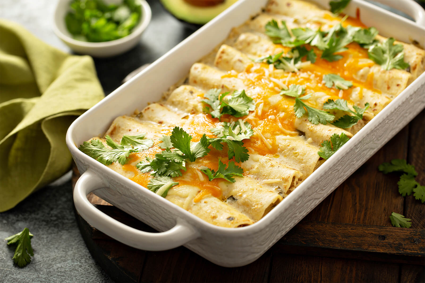 Frisch gebackene cremige Hähnchen-Enchiladas mit geschmolzenem Käse und Koriander in einer weißen Auflaufform mit Griffen