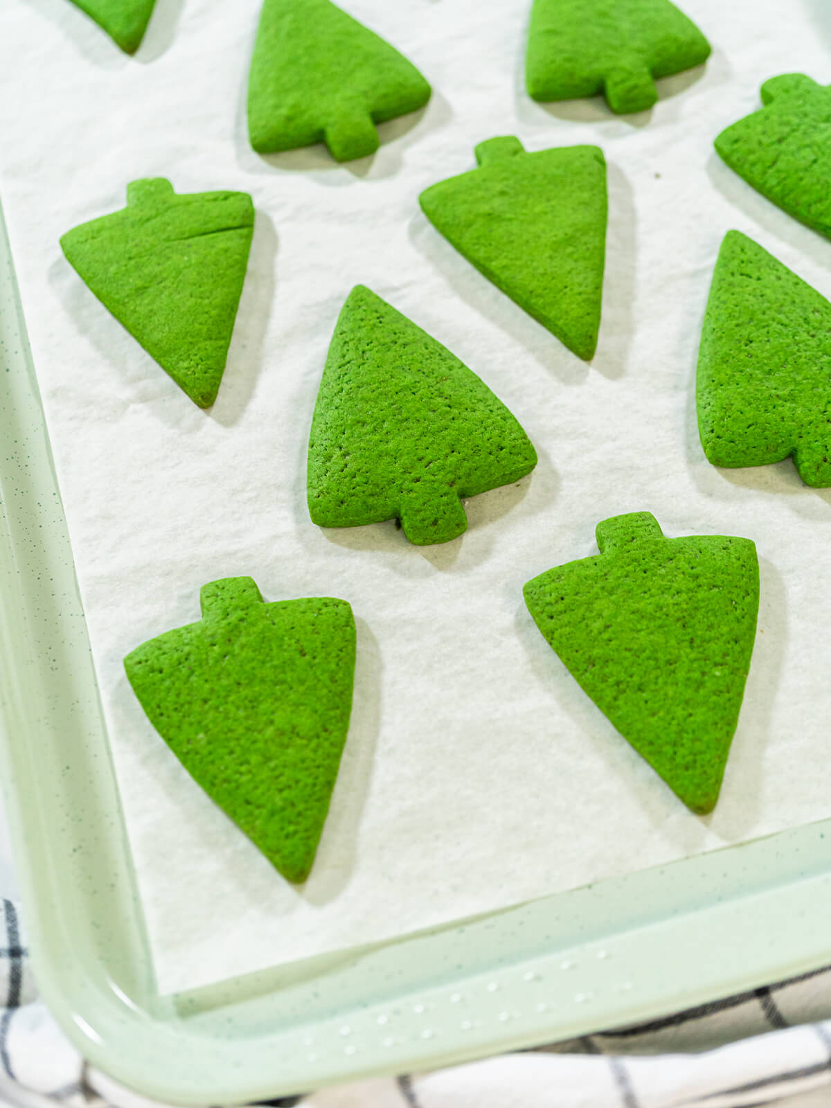 Fertig gebackene grüne Lebkuchen-Tannenbäume in Reihen auf einem Backblech