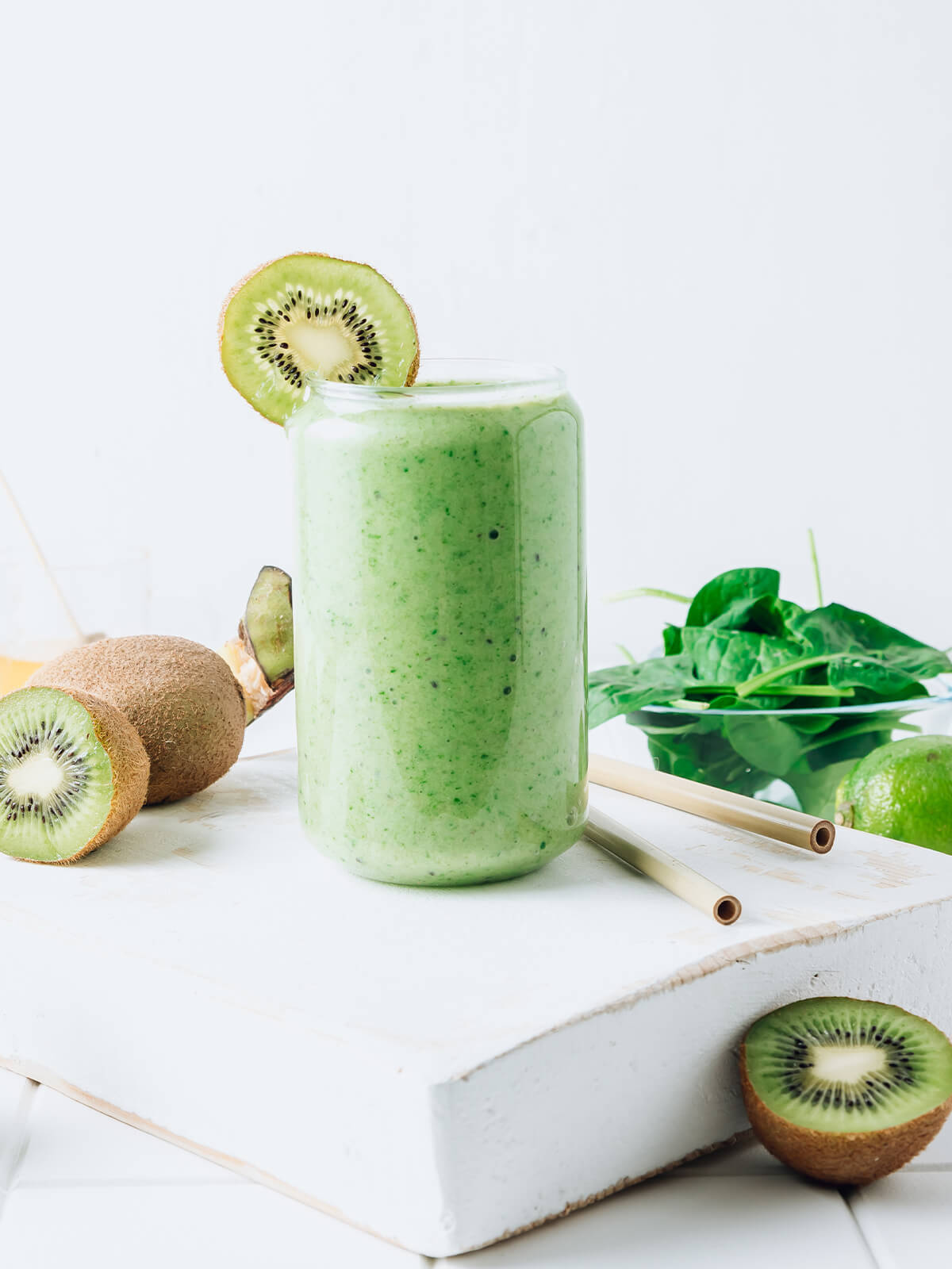 Cremiger grüner Smoothie mit Banane, Kiwi und Spinat im Glas, garniert mit einer Kiwischeibe, umgeben von frischem Obst und Spinat