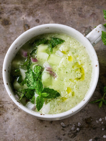 Kalte Gurken-Gazpacho mit Minze in einer weißen Tasse, garniert mit Gurkenwürfeln, roten Zwiebeln, frischer Minze und Olivenöl
