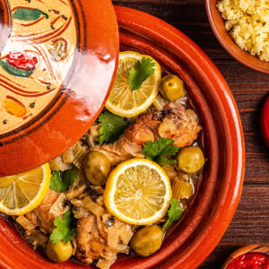 Marokkanische Hähnchen-Tajine mit grünen Oliven, Salzzitronen und Koriander in der Tajine, dazu Couscous und Harissa