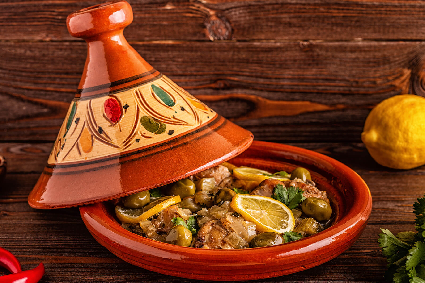Seitenansicht einer marokkanischen Tajine mit spitzem Deckel, daneben eine frische Zitrone auf hellem Tisch