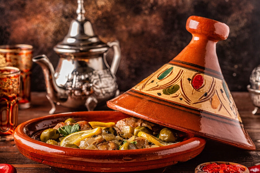 Stimmungsvolle Seitenansicht der Hähnchen-Tajine mit einer silbernen Teekanne im Hintergrund